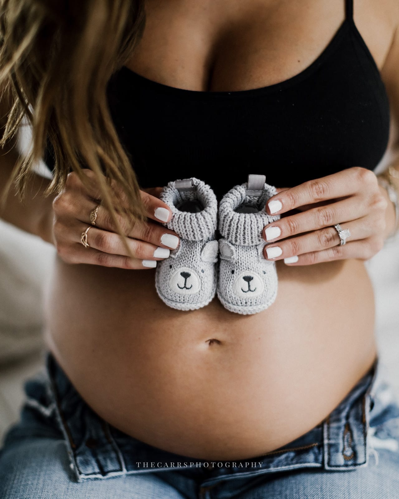 mom holds baby shoes over pregnant belly - cleveland maternity photographer in-home maternity session