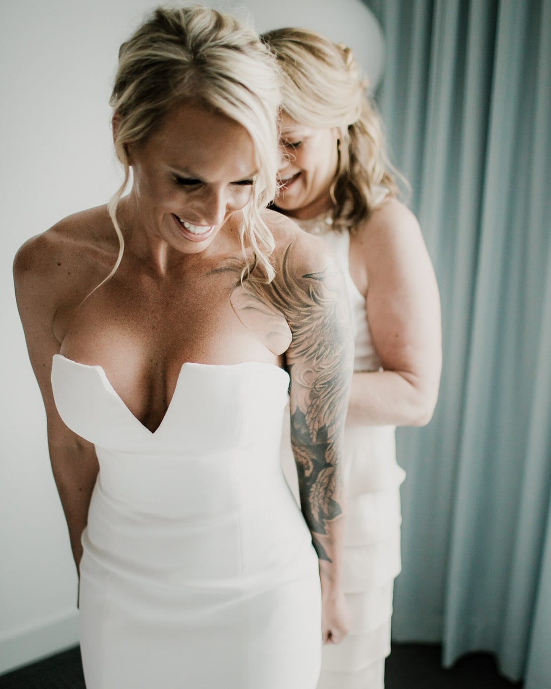 bride laughs as she gets help with dress at Juniper Rooftop Wedding