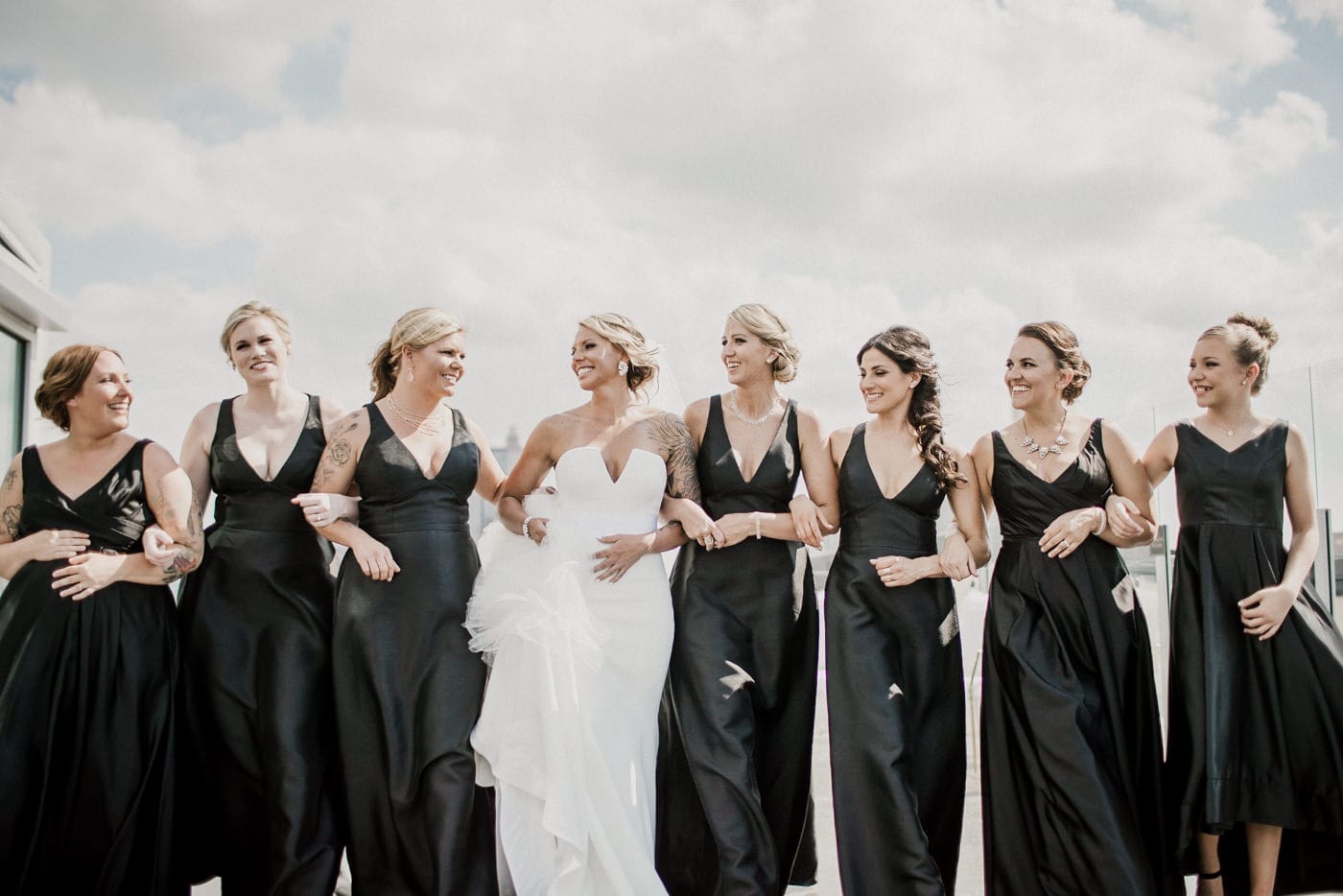 bride and bridesmaids link arms and smile at Juniper Rooftop Wedding