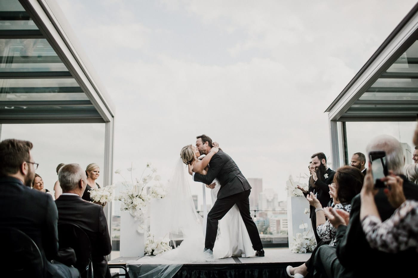 bride and groom first kiss with city outline in background at Juniper Rooftop Wedding