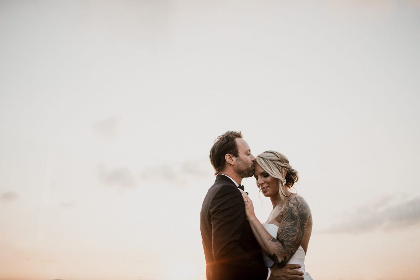 groom kisses brides forehead at golden hour at Juniper Rooftop Wedding