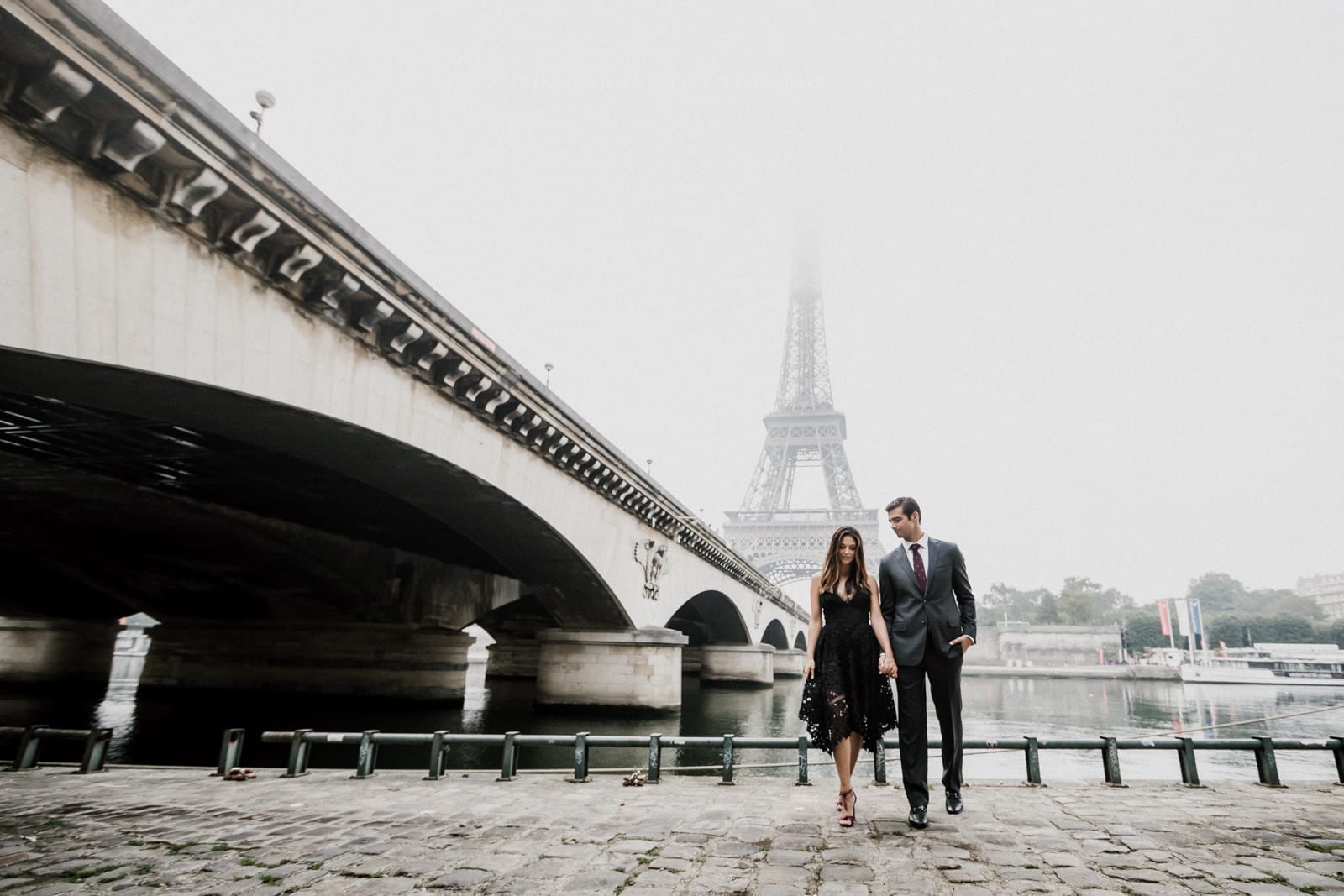 couple holds hands with Eiffel Tower in the distance by Paris Engagement Photographer