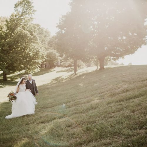 bride and groom walking up grassy hill by Dayton Ohio Photographer Kera Estep