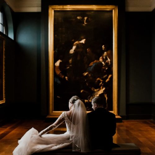 bride and groom sitting on bench in front of large piece of art by Dayton Ohio Photographer Kera Estep