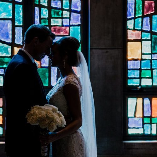 bride and groom embrace in front of stained glass window by Dayton Ohio Photographer Kera Estep