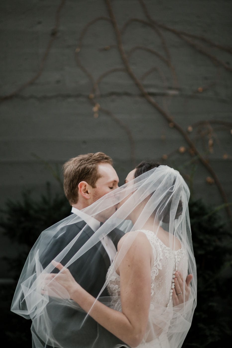 bride and groom kiss while bride's veil blows in wind at black tie winter wedding