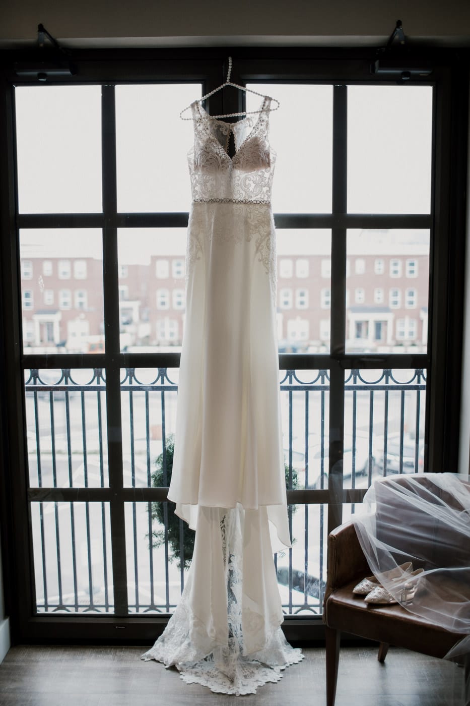 lace wedding gown hanging in window at black tie winter wedding