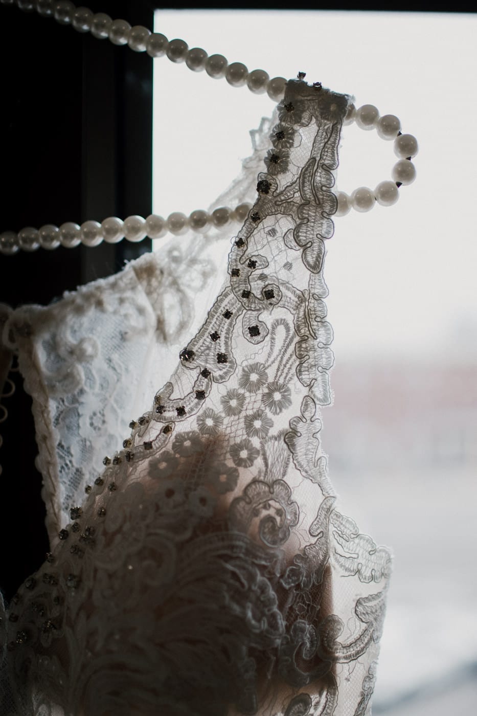 close up of lace on wedding gown hanging in window at black tie winter wedding