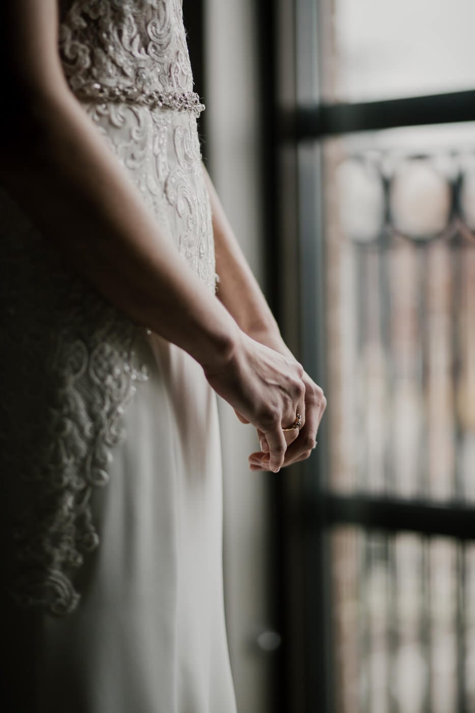 bride stands at window hands grasped at black tie winter wedding