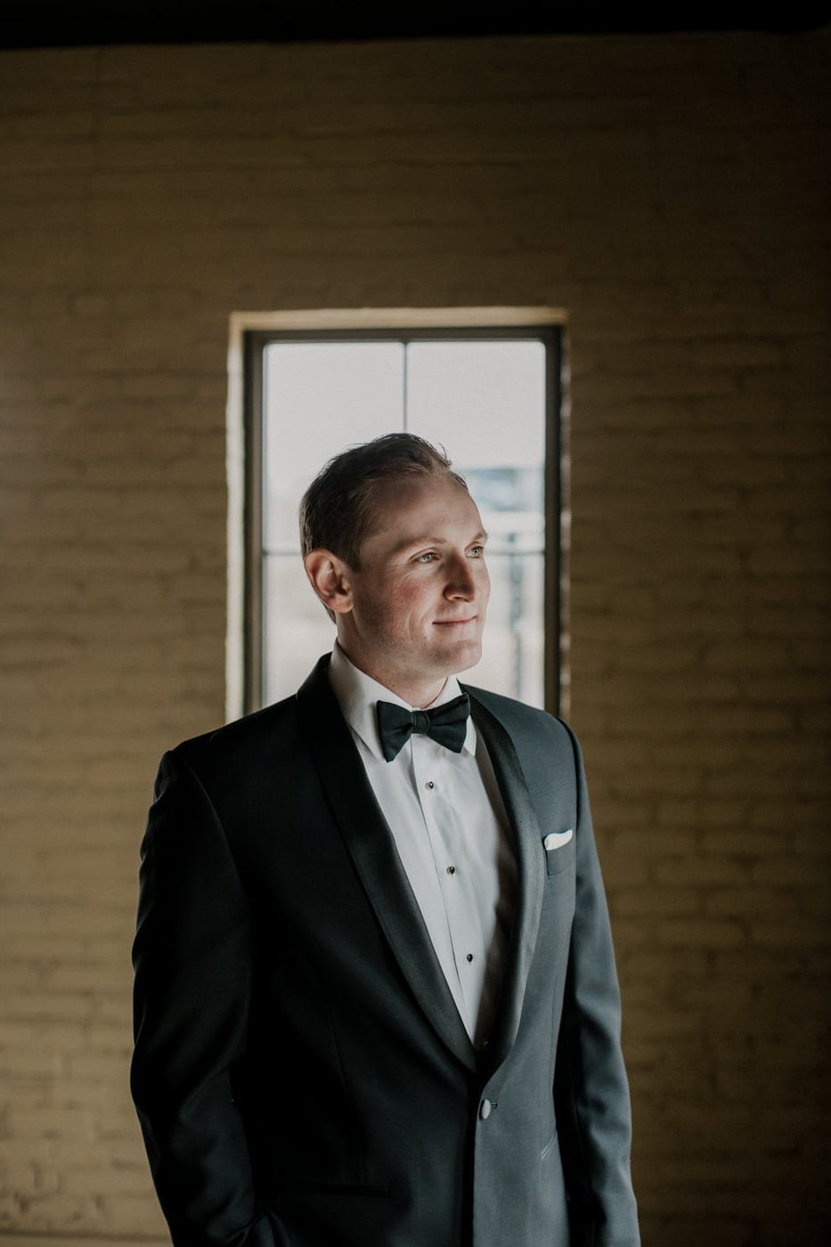 close up of groom looking out window at black tie winter wedding