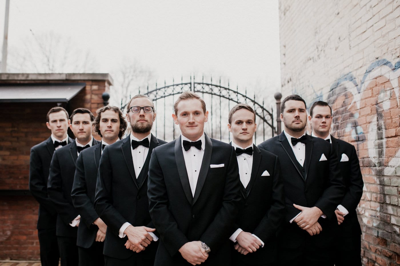 groom and groomsmen stand together hands folded in front at black tie winter wedding