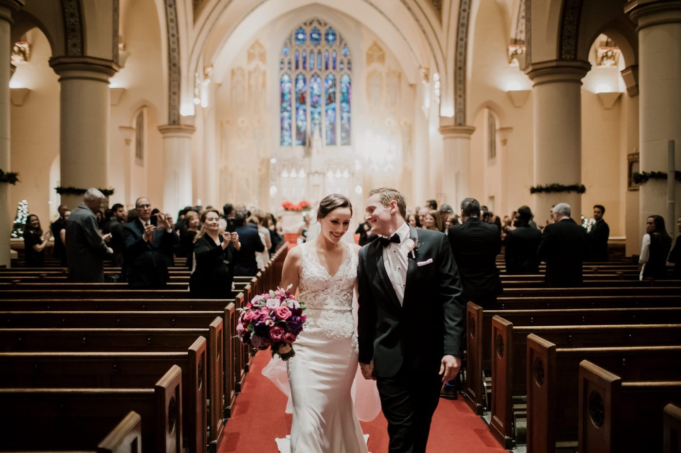 bride and groom walk out of church at black tie winter wedding