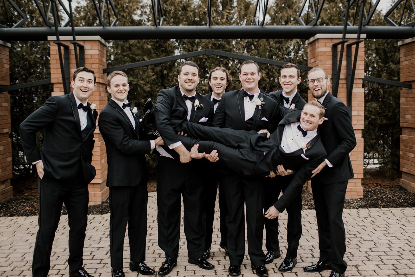 groomsmen hold up groom at black tie winter wedding