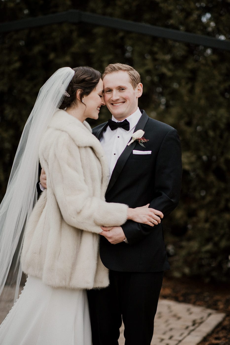 groom smiles at while bride puts her forehead on cheek at black tie winter wedding