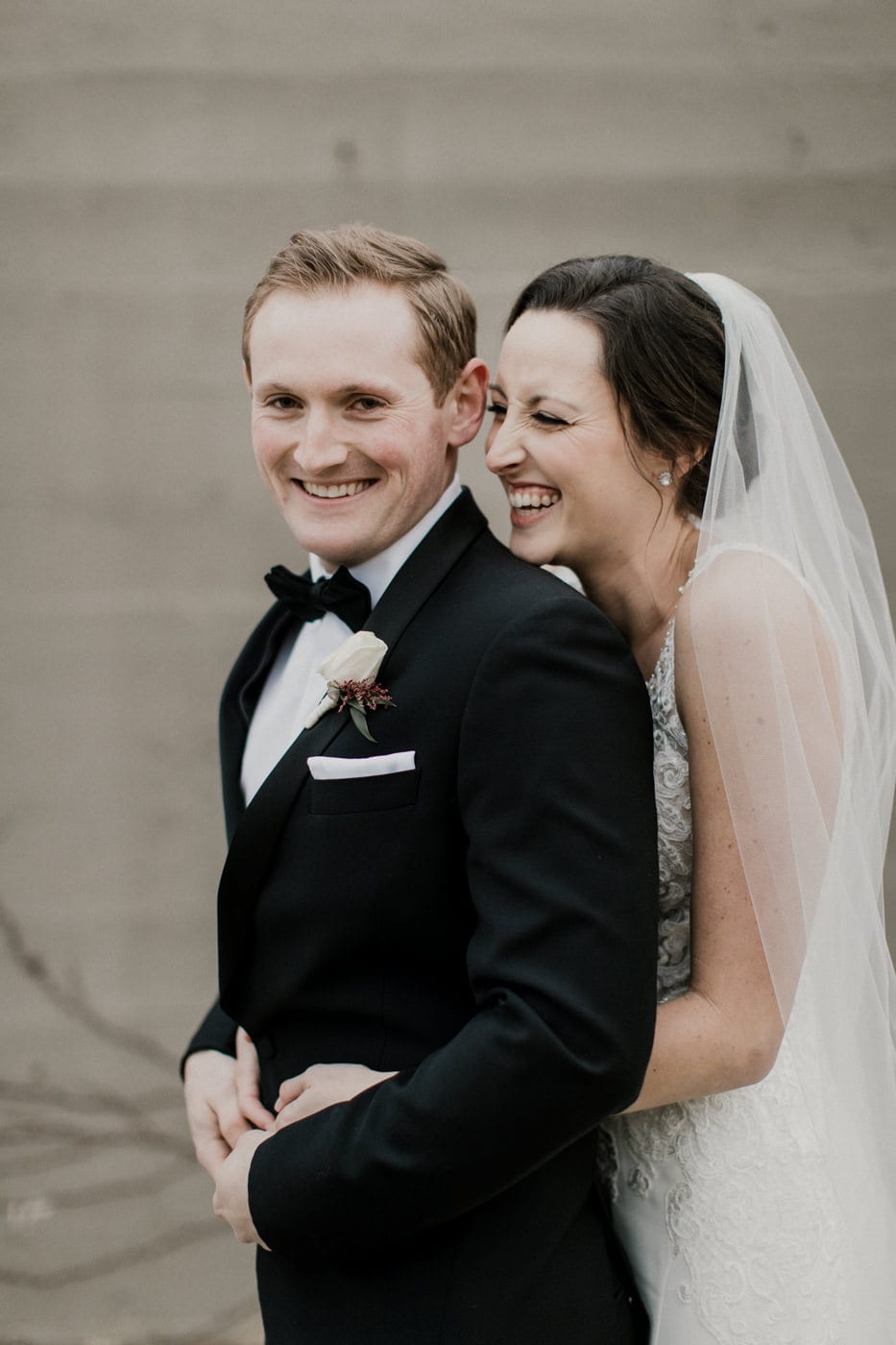 bride laughs while embracing groom at black tie winter wedding