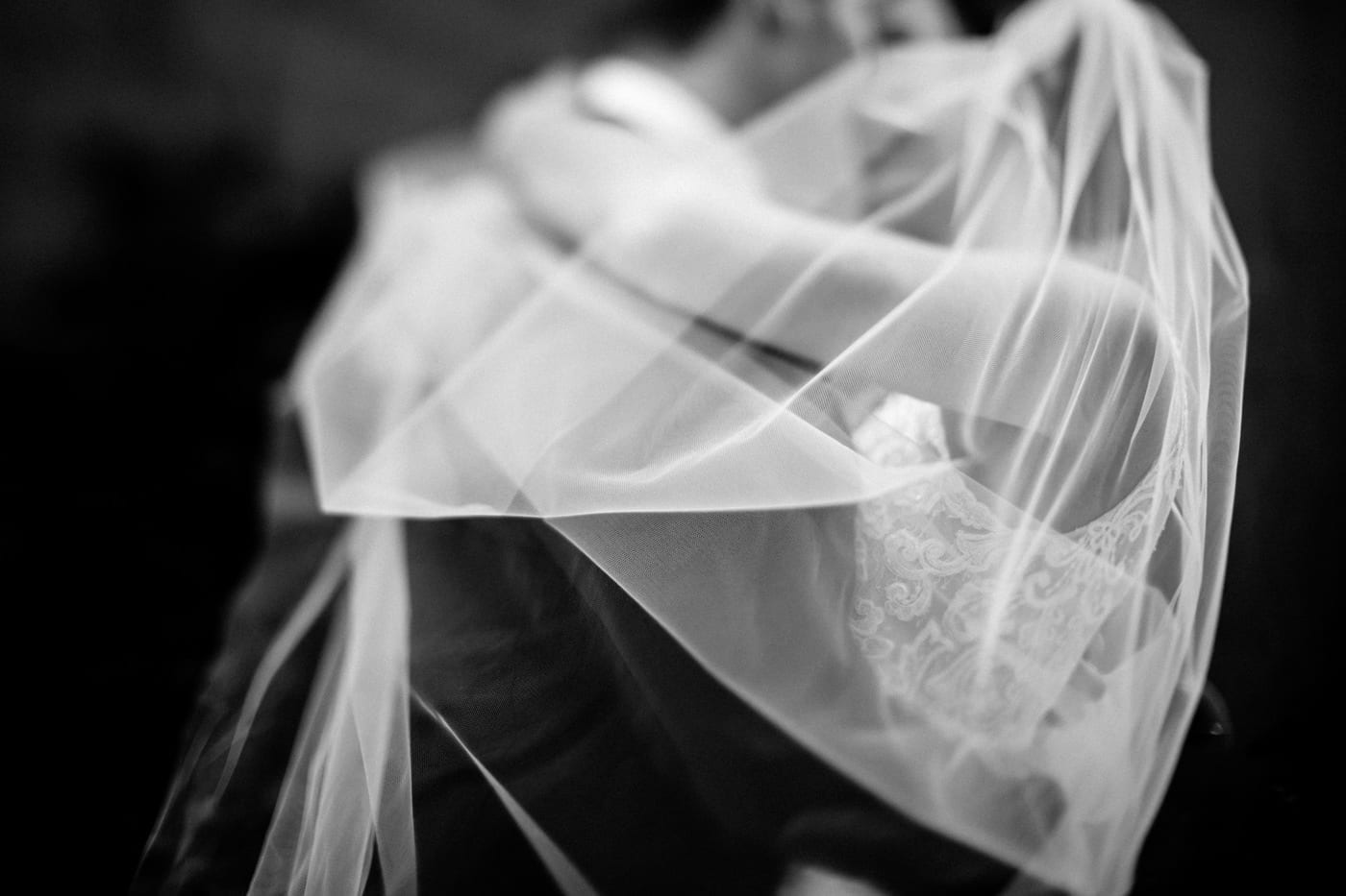 close up of bride and groom kissing with veil wrapped around them at black tie winter wedding