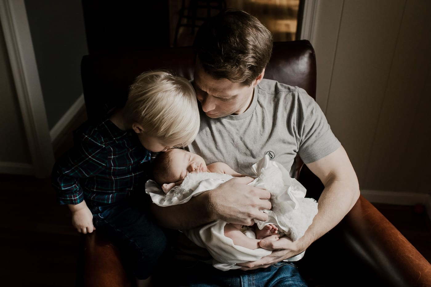 dad holding baby brother while older brother kisses his forehead - in-home newborn session