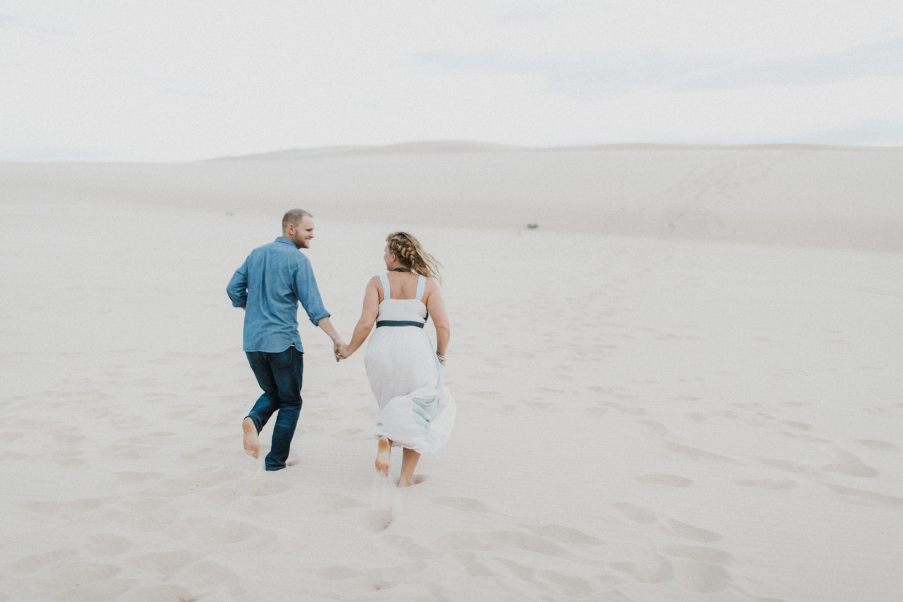 couple holds hands and walks on sand dunes at Family Portrait Session Silver Lake Sand Dunes - Destination Photographer