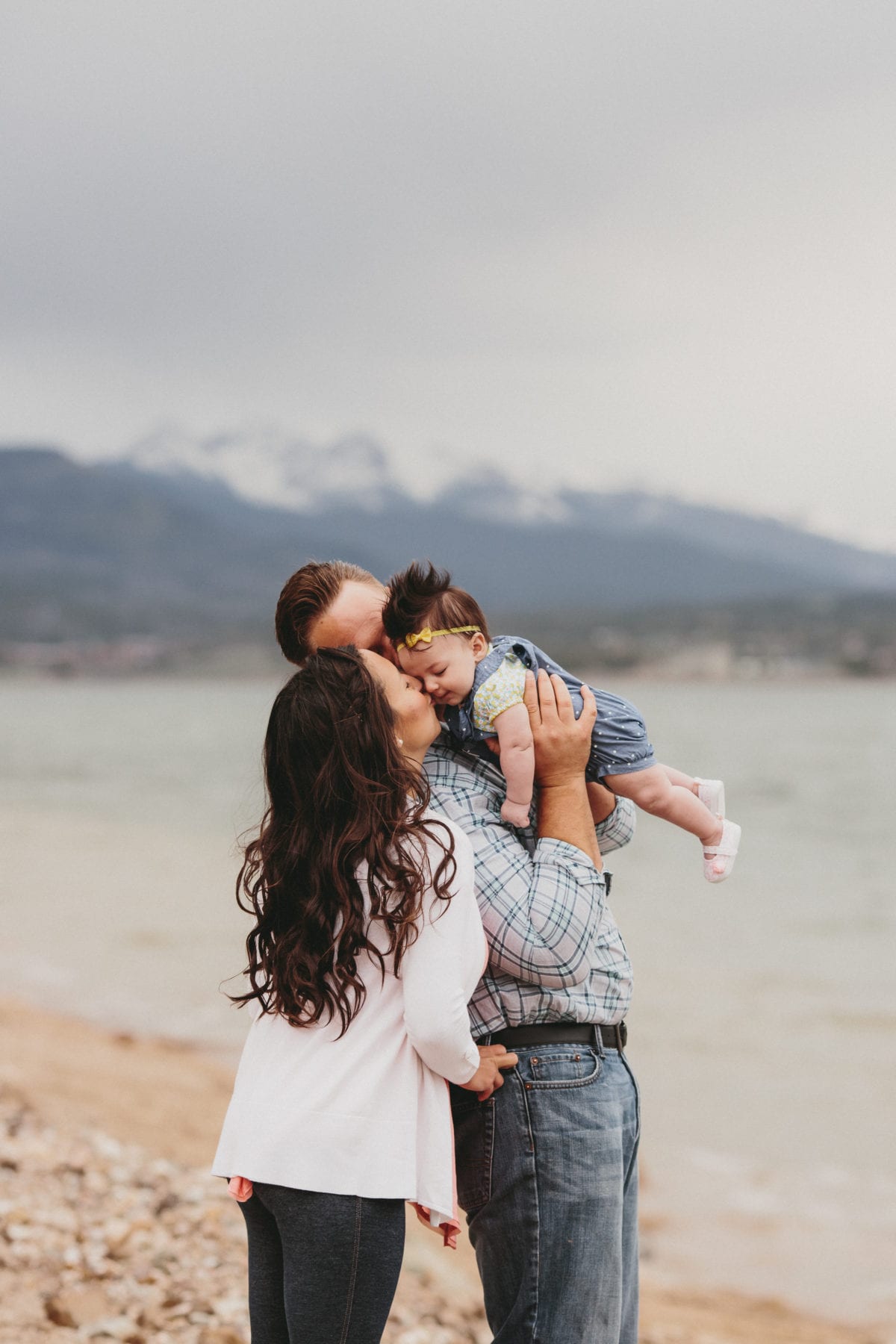 dad holds daughter while mom kisses her forhead at Grand Lake Colorado Family Portraits - Destination Photographer