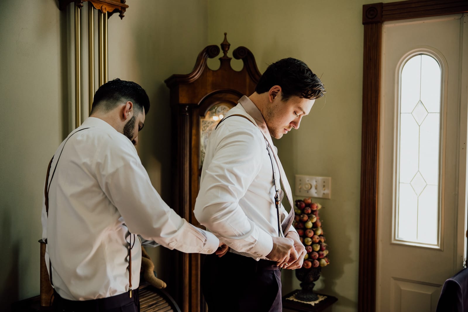 best man helps groom fasten suspenders