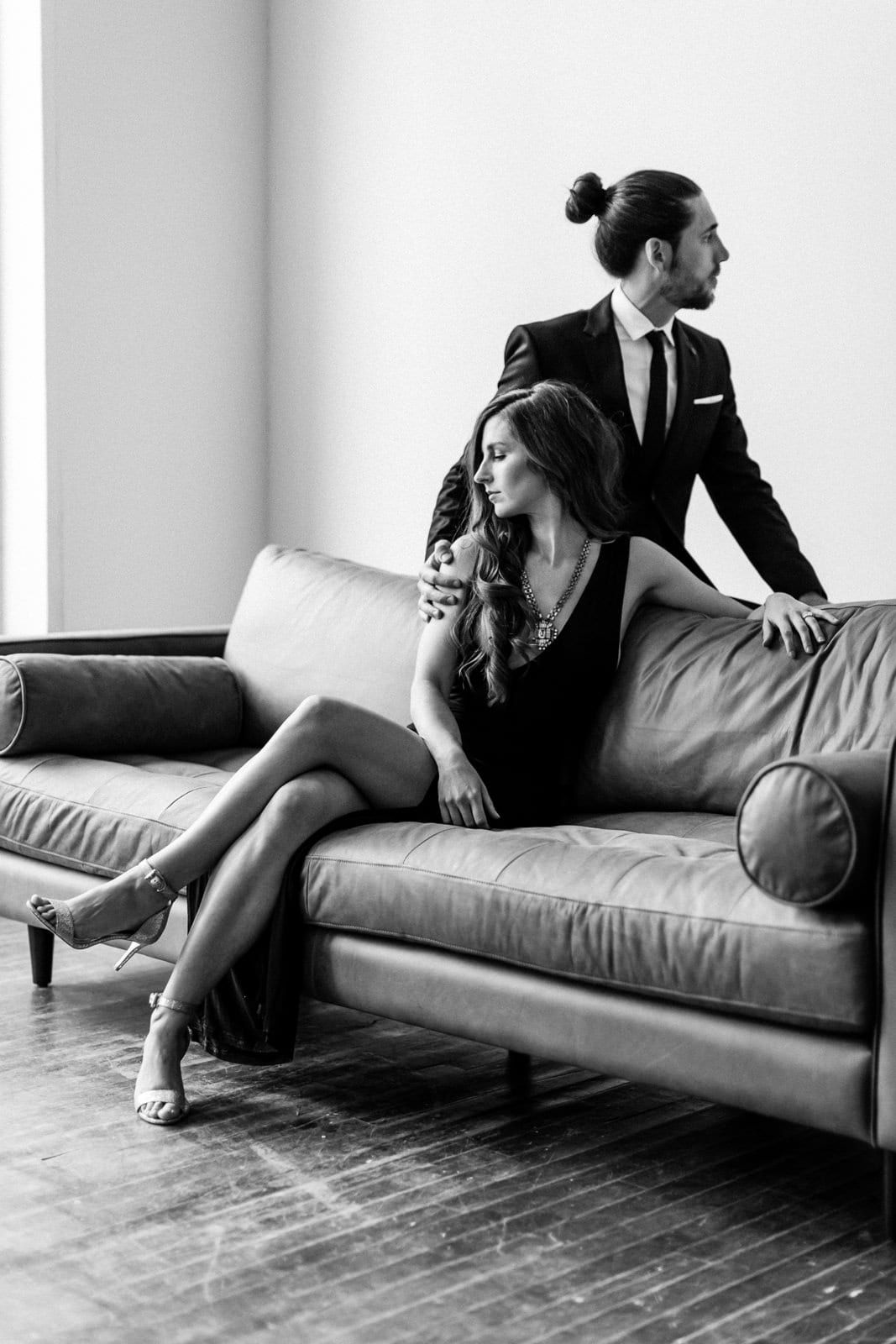couple looks away and sits on couch in engagement shoot