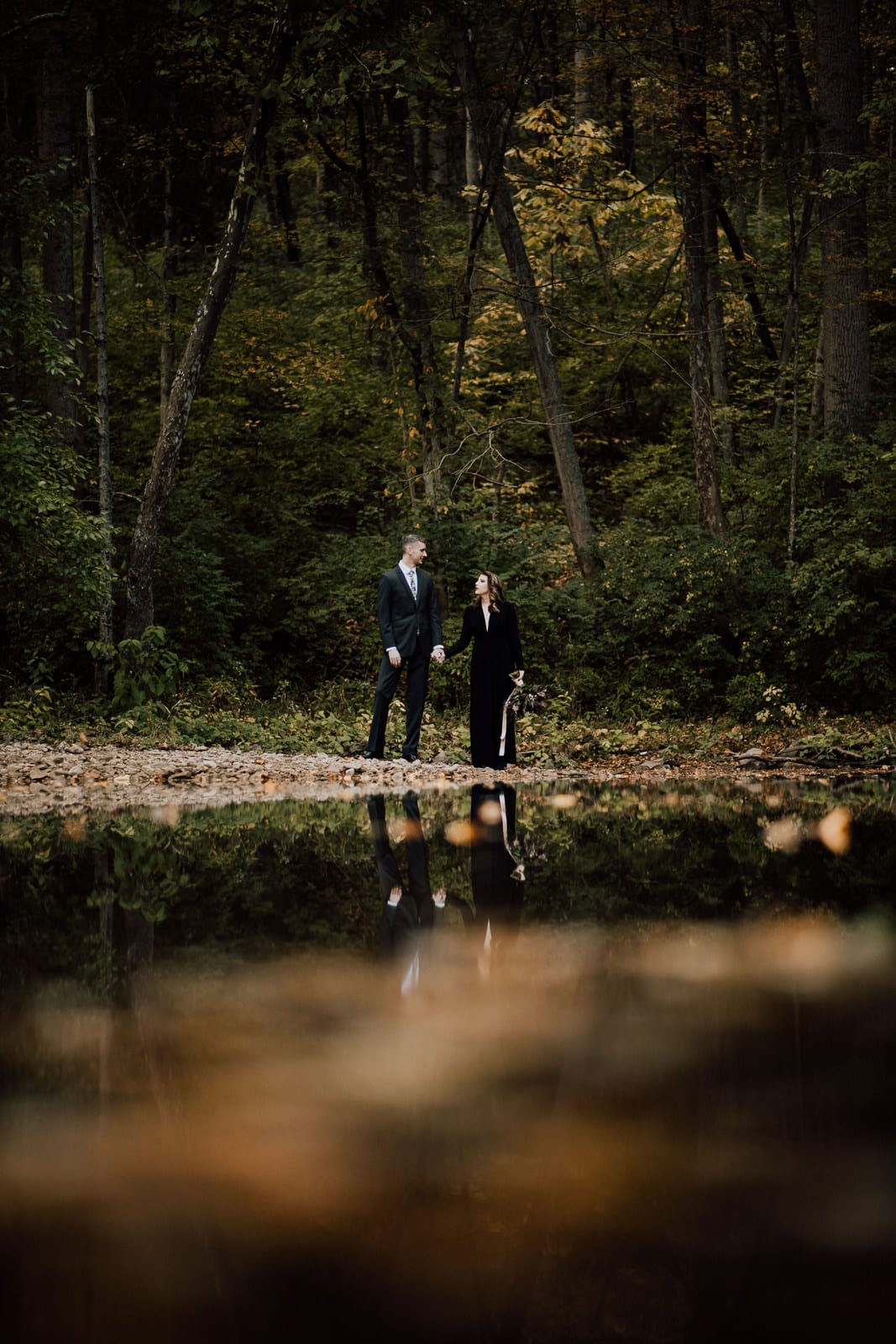 Bride and groom hold hands on the edge of a river