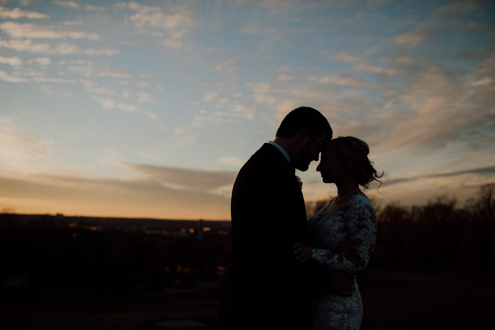 Bride and groom nuzzle in front of sunset