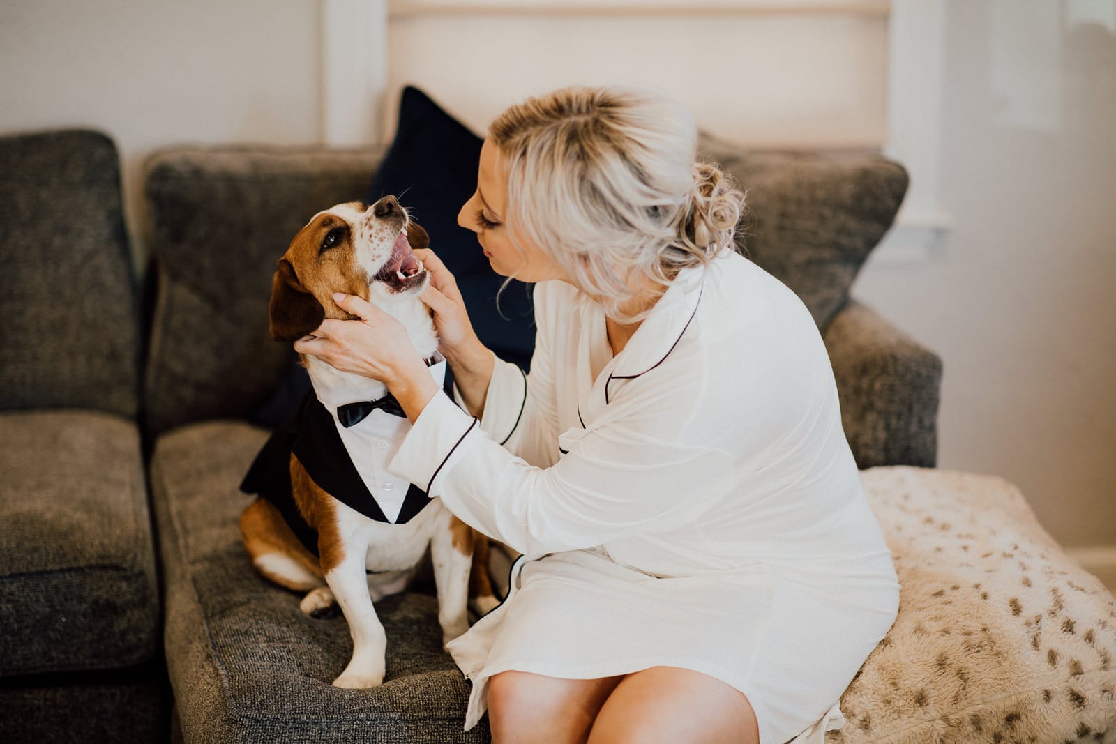 Bride smiles and plays with puppy in tuxedo