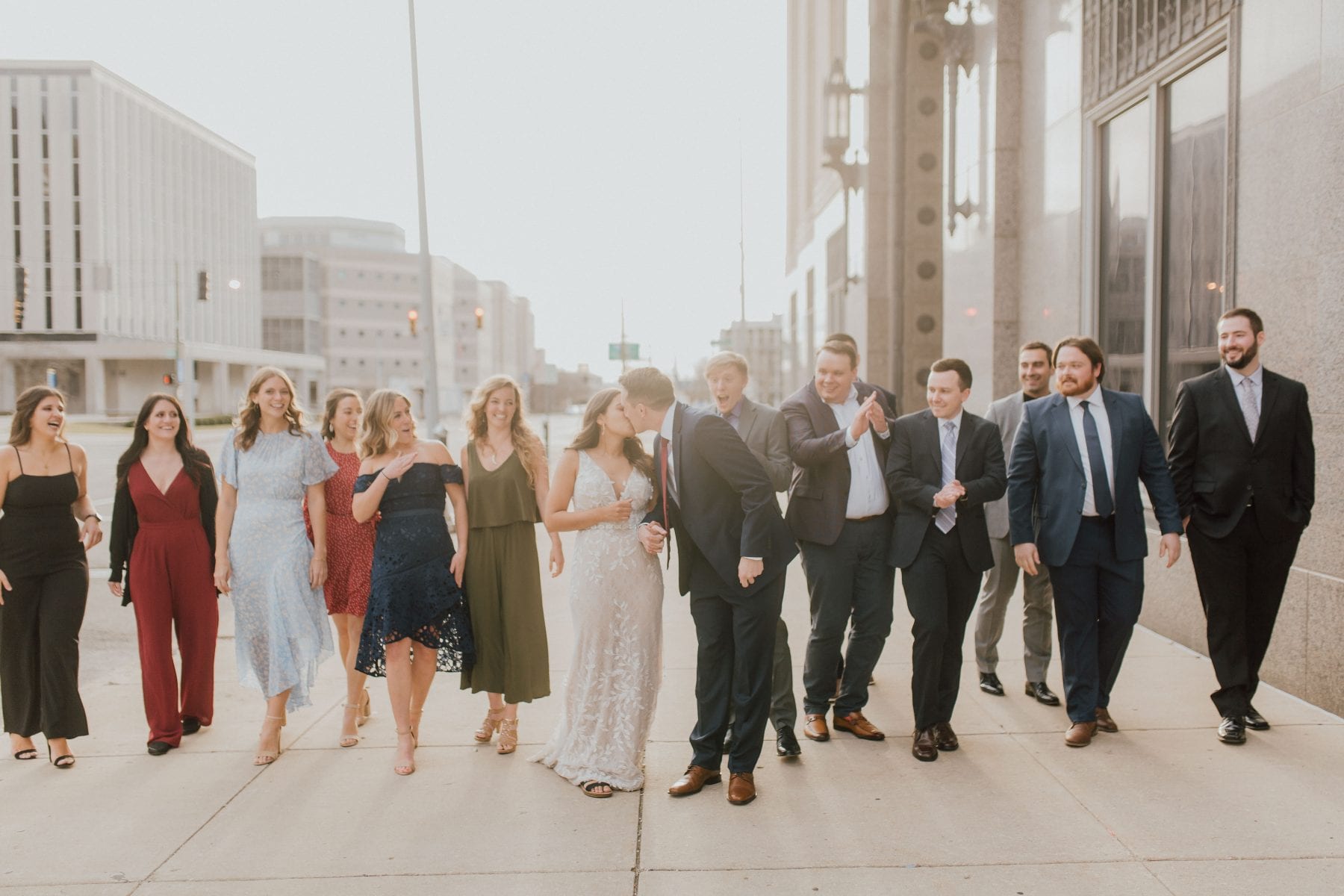 Bride and groom kiss while walking with bridal party